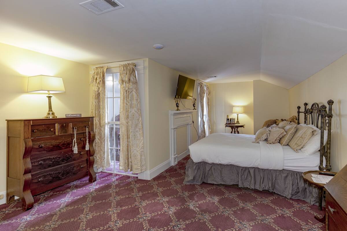 A bedroom with a bed, dresser, and a fireplace.