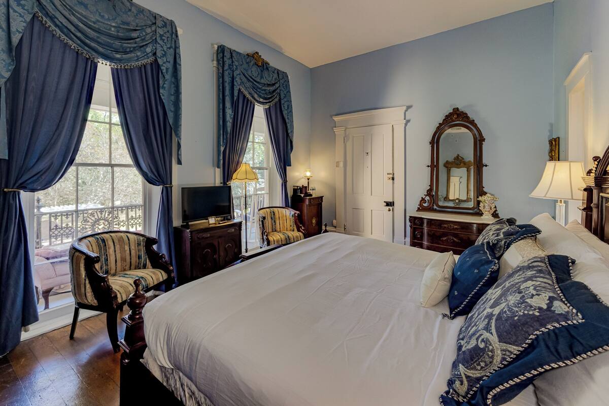 A bedroom with a large bed, a chair, a dresser, and a mirror.