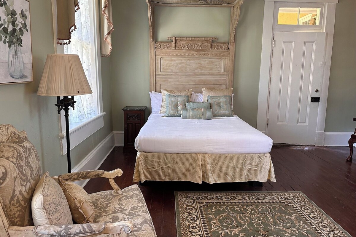 A bedroom with a large bed, a wooden headboard, a door, a chair, and a floor lamp.