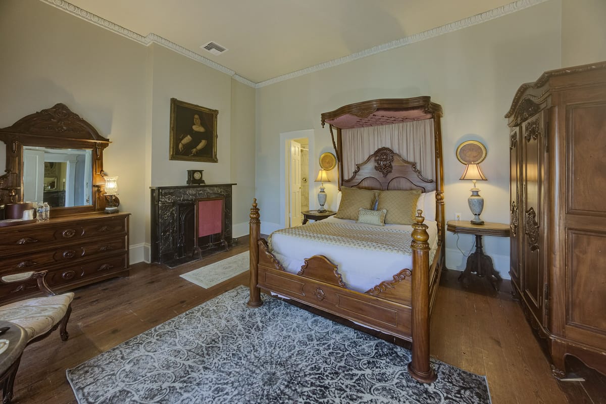 A bedroom with a four-poster bed, wooden furniture, a mirror, and a fireplace.