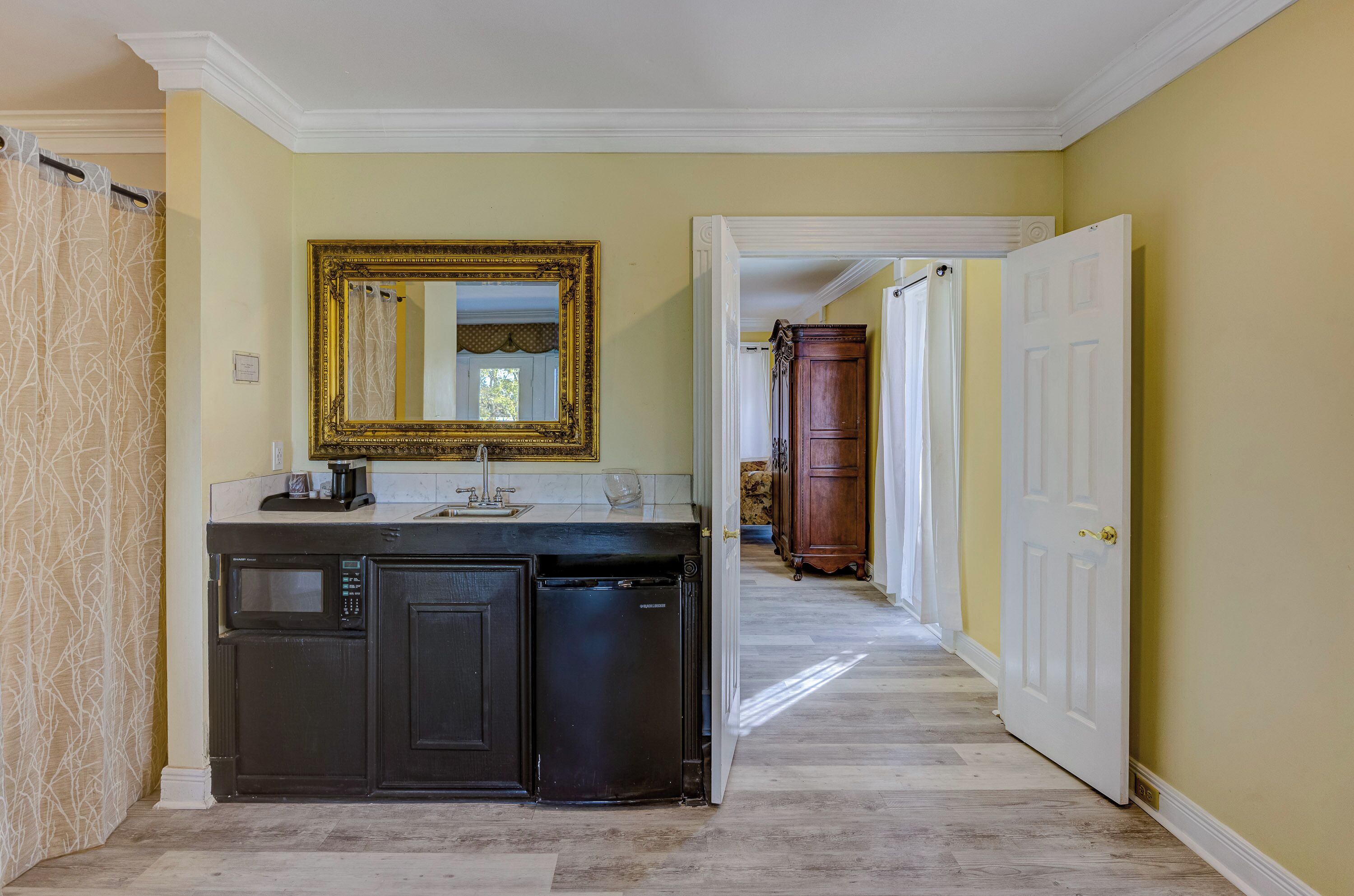 A kitchen with a black dishwasher, a microwave, and a sink. There is a large mirror above the sink and a wooden cabinet in the background.