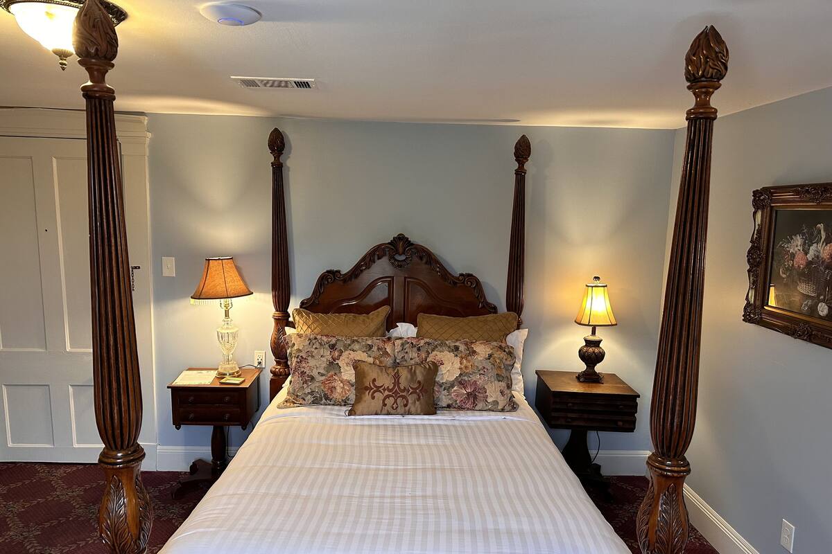 A four-poster bed with a floral bedspread, two bedside lamps, and a framed picture on the wall.