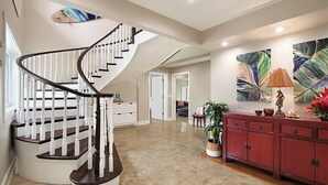 A spacious interior with a curved staircase, a red cabinet, and a large abstract painting. - Mala Nani Hale Kiahuna Golf Course By Suite Paradise (Koloa)