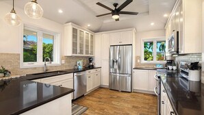 A modern kitchen with white cabinets, a stainless steel refrigerator, and a black countertop. - Mala Nani Hale Kiahuna Golf Course By Suite Paradise (Koloa)