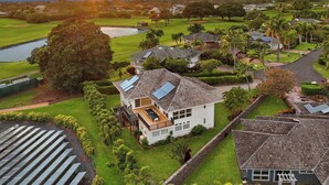 A residential area with a house featuring a balcony, solar panels, and a view of a golf course and water body. - Mala Nani Hale Kiahuna Golf Course By Suite Paradise (Koloa)