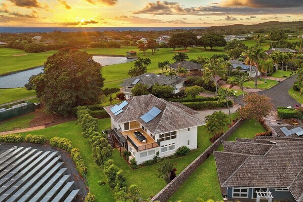Zona residencial con una casa que tiene balcón, paneles solares y vista a un campo de golf y un cuerpo de agua.
