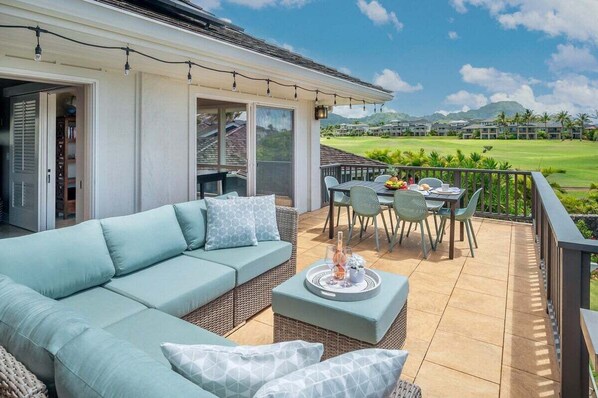 A balcony with a light blue sofa, wicker chairs, and a dining table set with a fruit bowl and a tray.