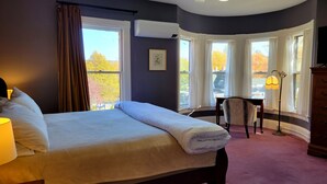A bedroom with a large bed, a desk, a chair, and a dresser. There are multiple windows providing views of the outside. - The Elizabeth Inn and Restaurant (Bethel)
