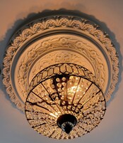 A chandelier with a geometric design and multiple crystal elements, set within an ornate, circular ceiling medallion.