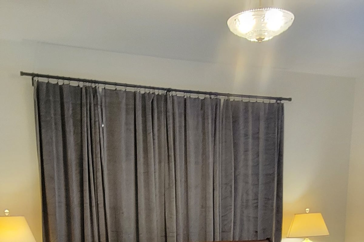 Une chambre à coucher avec un lit en bois, deux tables de chevet avec des lampes, un rideau gris et un lustre.