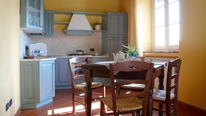 A kitchen with a dining table and chairs, a stove, and a window with curtains. - "encantea" lovely country house - apartment "Timo" (Lucca)