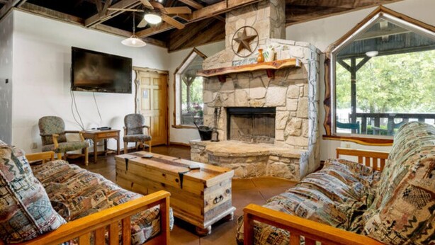 Una sala de estar acogedora con chimenea de piedra, muebles de madera y ventanas amplias.