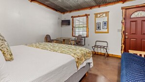Una habitación con cama, escritorio, silla, una mesita y una puerta.