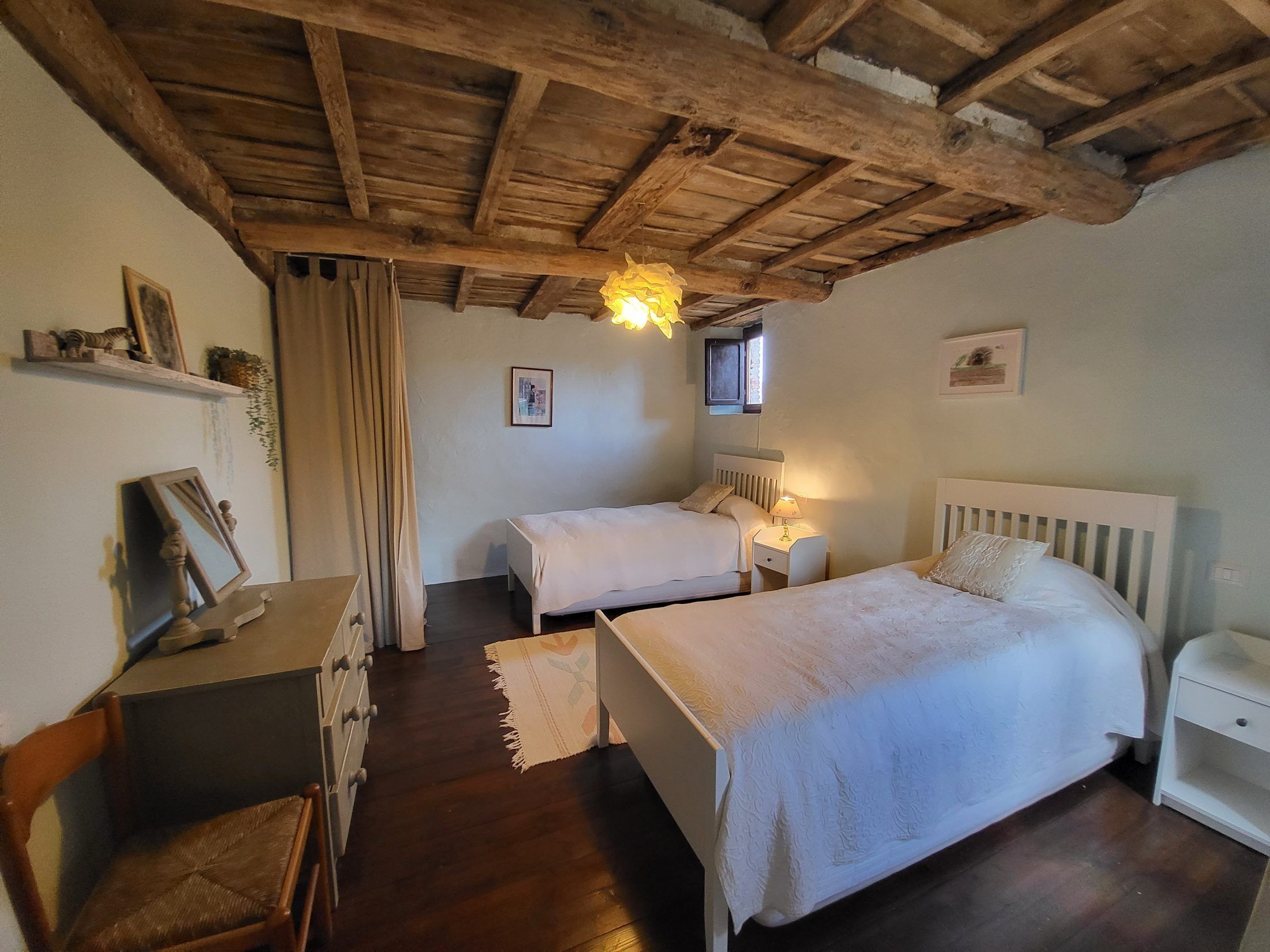 Een slaapkamer met twee bedden, houten balken in het plafond, een bureau met stoel en een raam.