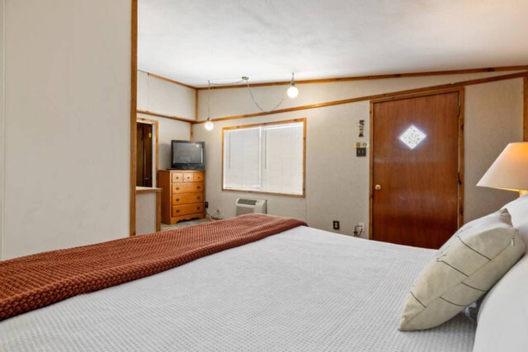 Een hotelkamer met een bed, een houten dressoir, een televisie, een raam en een deur.