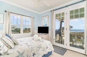 Une chambre avec un lit, une télévision et une vue sur la plage, accessible par une porte-fenêtre coulissante.