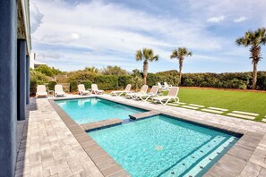 Une piscine rectangulaire bordée de carreaux, entourée de chaises longues blanches et d’une pelouse bien entretenue agrémentée de palmiers.
