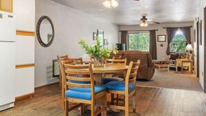 Un coin repas avec des chaises et une table en bois, un salon avec un canapé et un téléviseur, et un ventilateur de plafond.