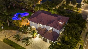 Una casa a due piani con tetto in tegole rosse, circondata da palme e una piscina.