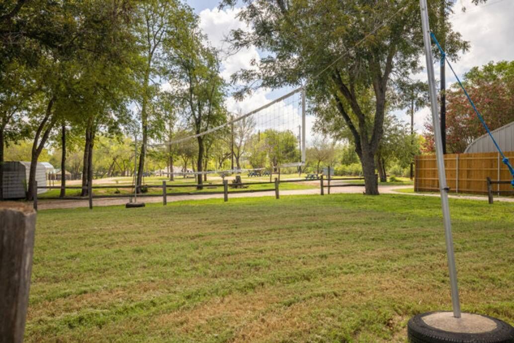 A park with a volleyball net, trees, and a picnic area.