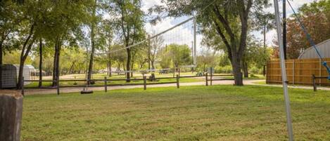 A park with a volleyball net, trees, and a picnic area.