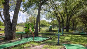 Un campo de mini golf con césped artificial verde, hoyos de madera y un carrito de golf mecánico grande.