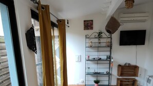 A hallway with a tiled floor, a wooden bench, a shelf with decorative items, and a television mounted on the wall. - The house around the fig tree (Aramon)