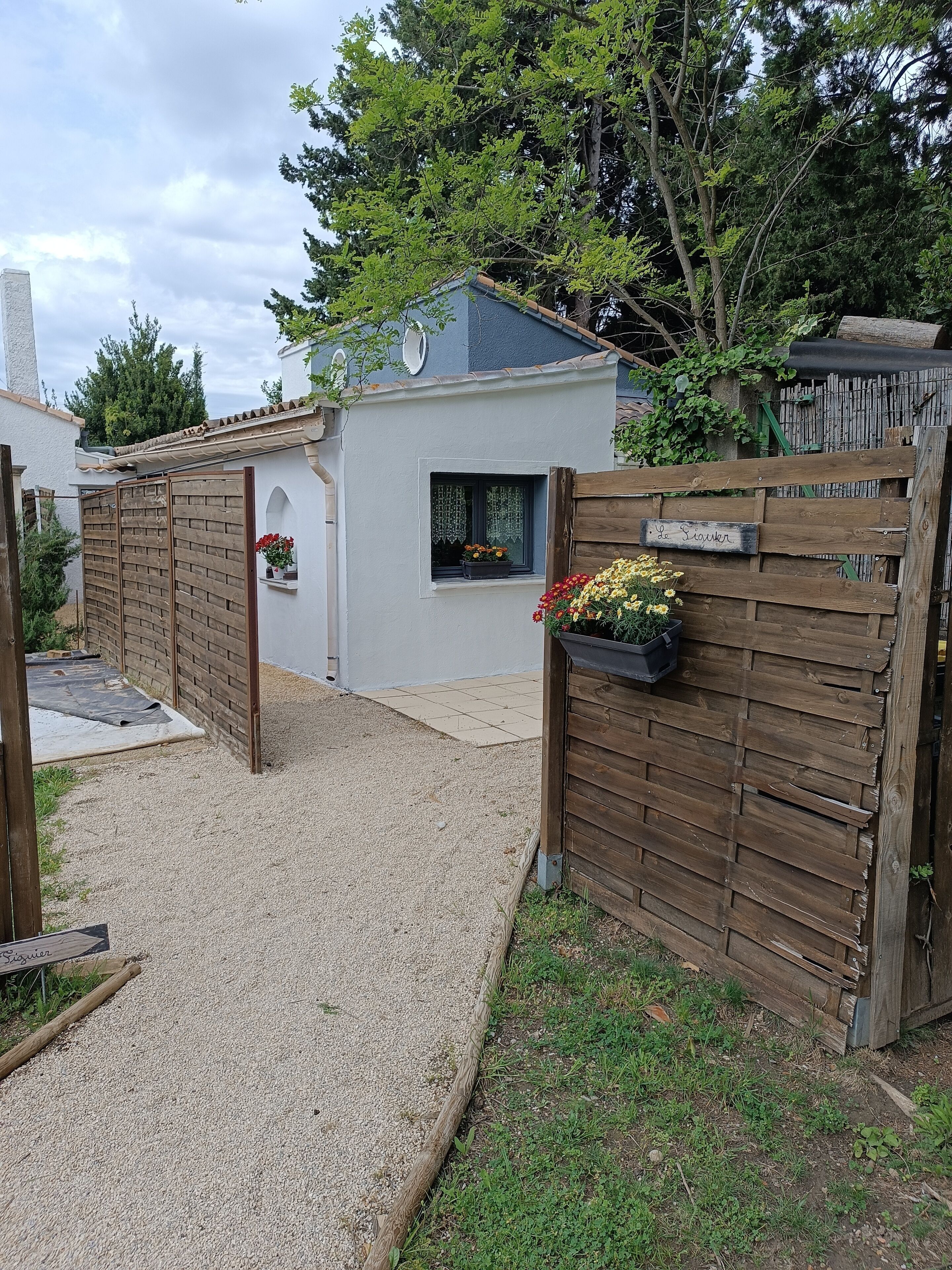 A residential property with a gravel driveway, a wooden gate, and a small garden area with potted plants.