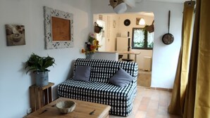 A cozy living room with a patterned sofa, a wooden coffee table, and a kitchen in the background. - The house around the fig tree (Aramon)