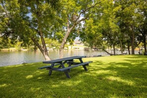 A picnic table in a grassy area with trees and a body of water in the background. - RV Site - Pull Through 33 (Burnet)