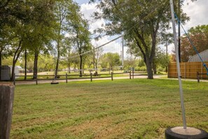 A park with a volleyball net, trees, and a picnic area. - RV Site - Pull Through 33 (Burnet)