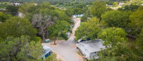 An aerial view of a rural area with scattered houses, a dirt road, and dense greenery.