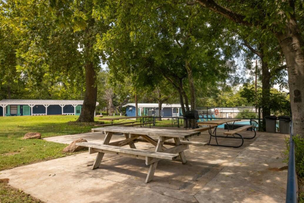 Un área de picnic al aire libre con mesas y una piscina al fondo.