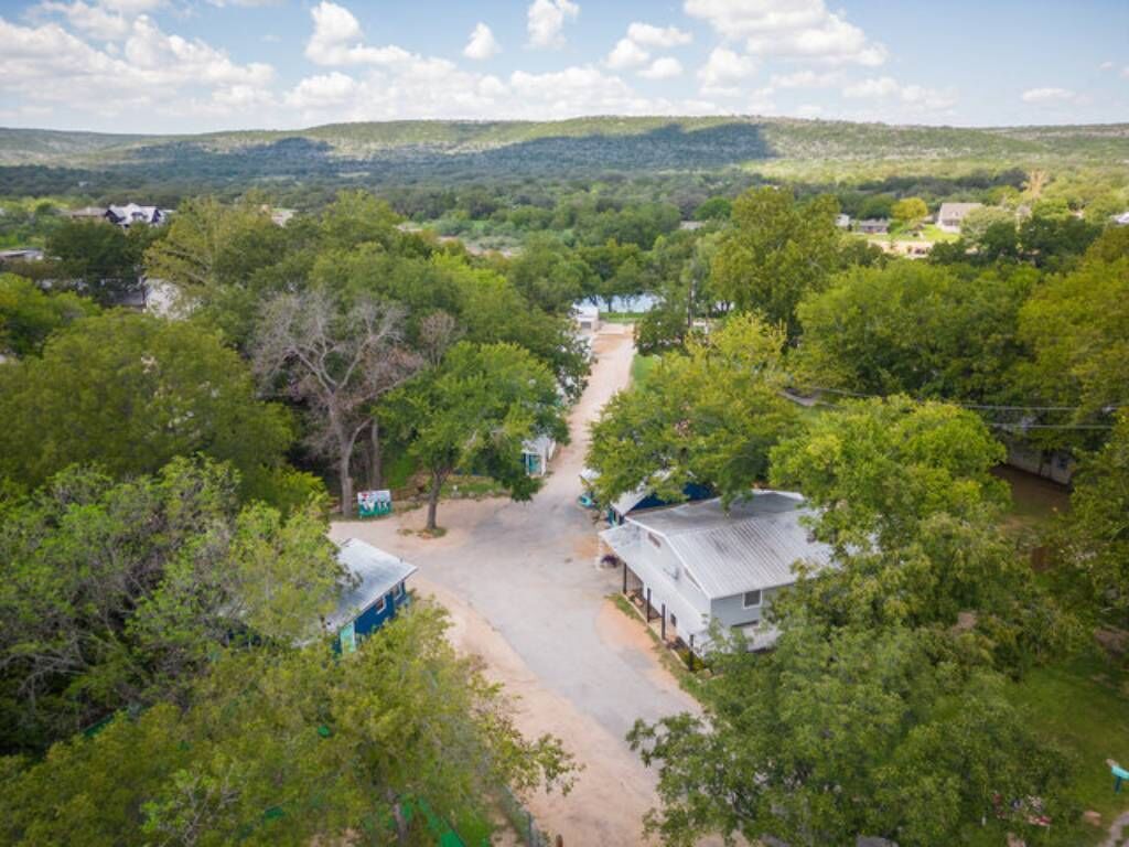 An aerial view of a rural area with scattered houses, a dirt road, and dense greenery.