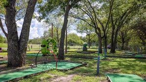 Un campo de mini golf con césped artificial verde, hoyos de madera y un carrito de golf mecánico grande.