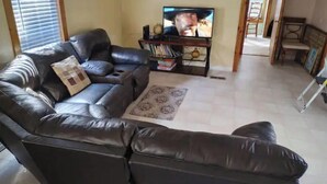 Ein Wohnzimmer mit einer schwarzen Ledersofa, einem Couchtisch, einem Fernseher und einem Bücherregal.