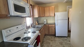 A kitchen with wooden cabinets, a white stove, a microwave, and a refrigerator.