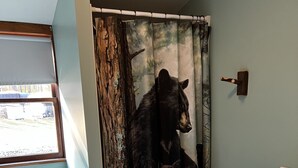 A bathroom with a toilet, a sink, and a shower curtain depicting a bear.