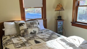 A bedroom with a large bed, two windows, a nightstand, and a lamp.