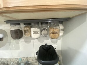 A kitchen shelf with jars labeled coffee, oats, sugar, tea, and brown sugar.
