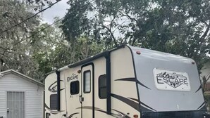 Una caravana blanca con la marca 'ESCAPE' estacionada en un camino de entrada residencial.