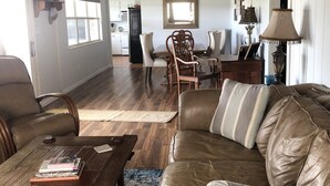 Een ruime woonkamer met een leren bank, een houten salontafel en een eethoek met stoelen en een tafel.
