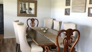 Een eetkamer met een houten tafel, gestoffeerde stoelen, een plafondventilator, een spiegel en lijstwerken aan de muur.