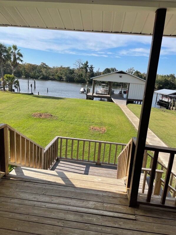 A wooden deck with a view of a lake, a covered area, and a small building.