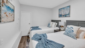 Une chambre d’hôtel avec deux lits, un tableau représentant des voiliers et une porte.