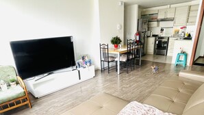 A living room with a flat-screen TV, a sofa, a dining table with chairs, a small kitchen area, and a pet. - New, comfortable and very well equipped apartment. (Quito)