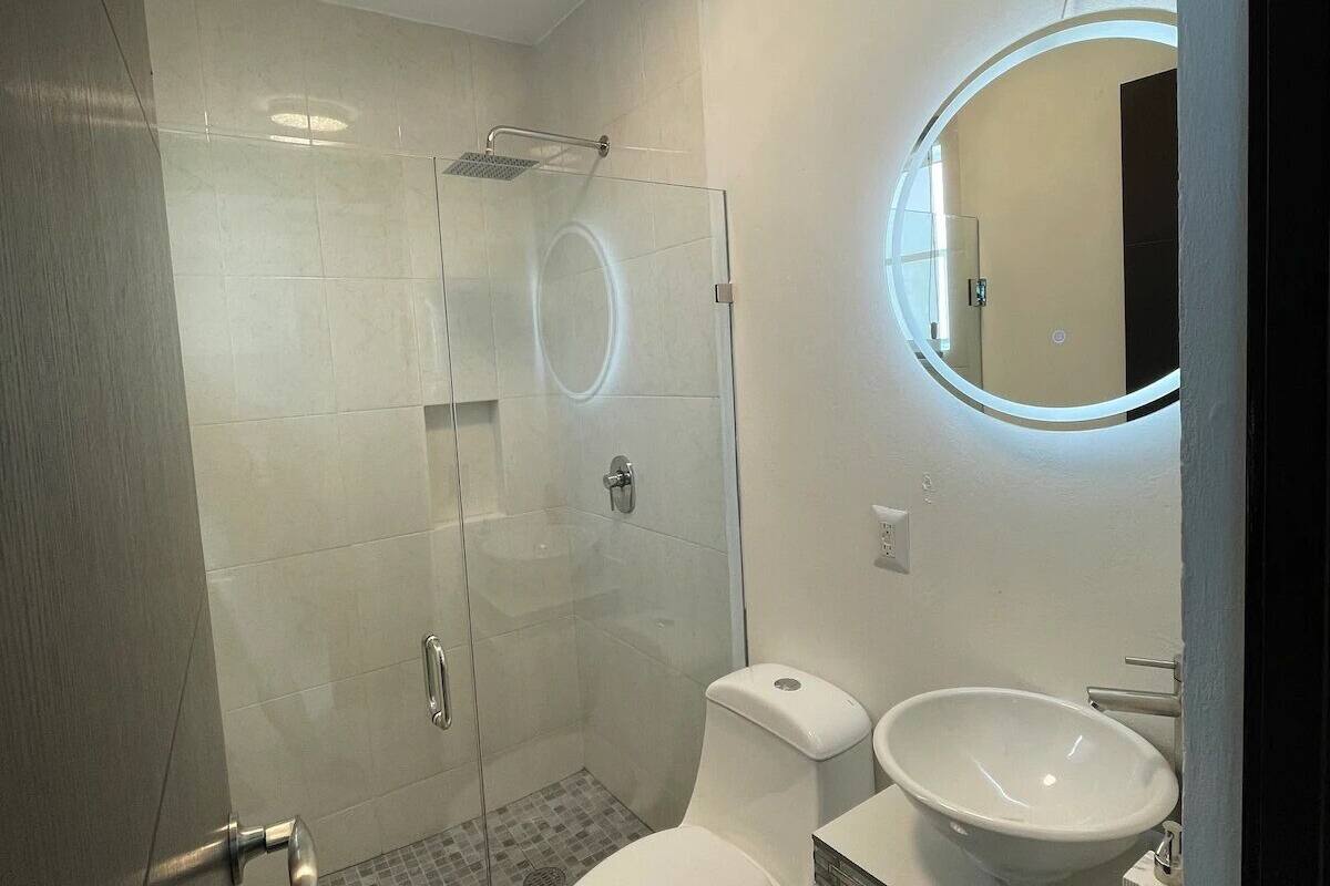 A modern bathroom with a glass-enclosed shower, a toilet, and a sink with a round mirror.