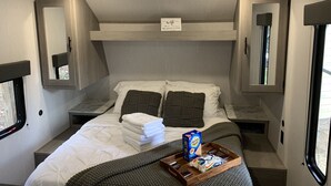 A compact RV bedroom with a bunk bed, a bedside table with a tray of snacks, and a window with a view.