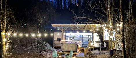 A campsite with a covered RV area, a fire pit, and string lights.