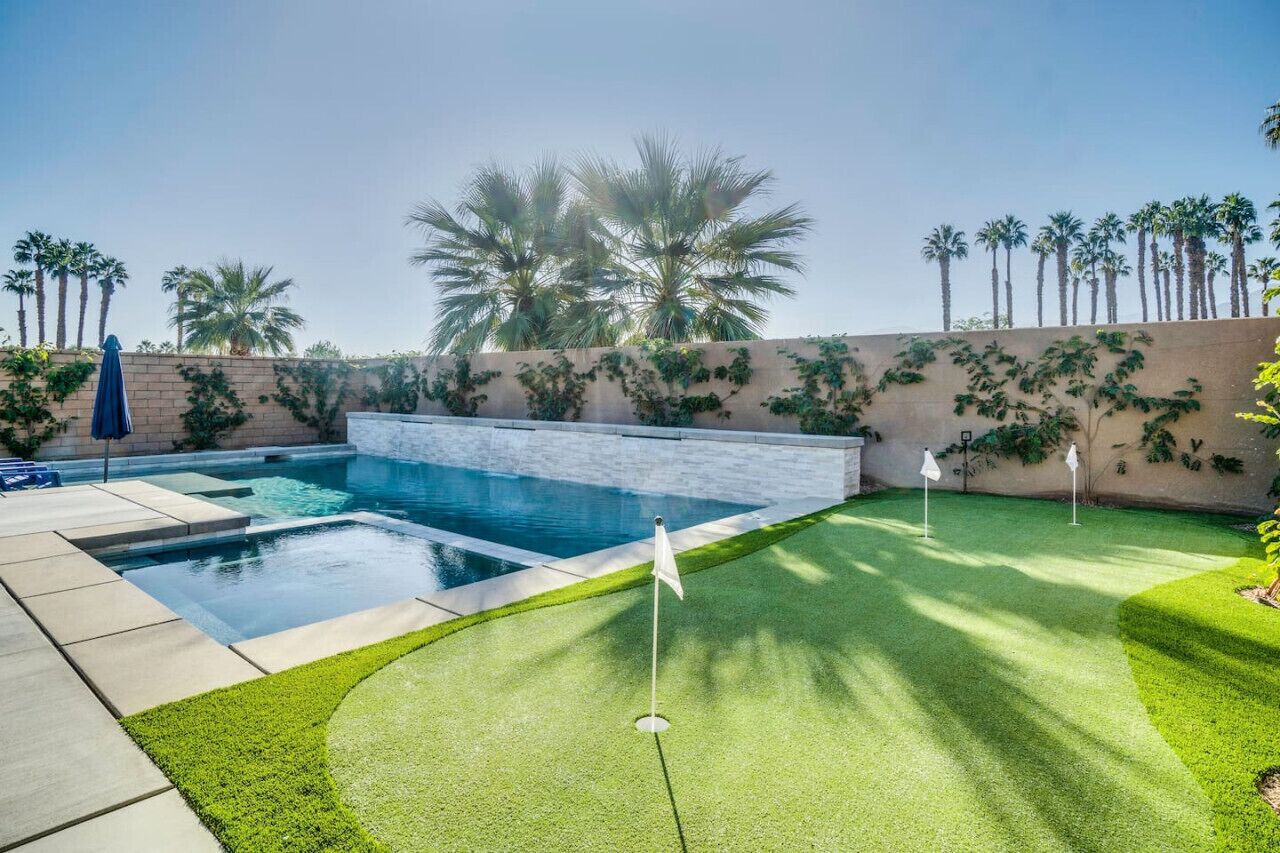 A swimming pool with a small putting green area, surrounded by palm trees and a stone wall.